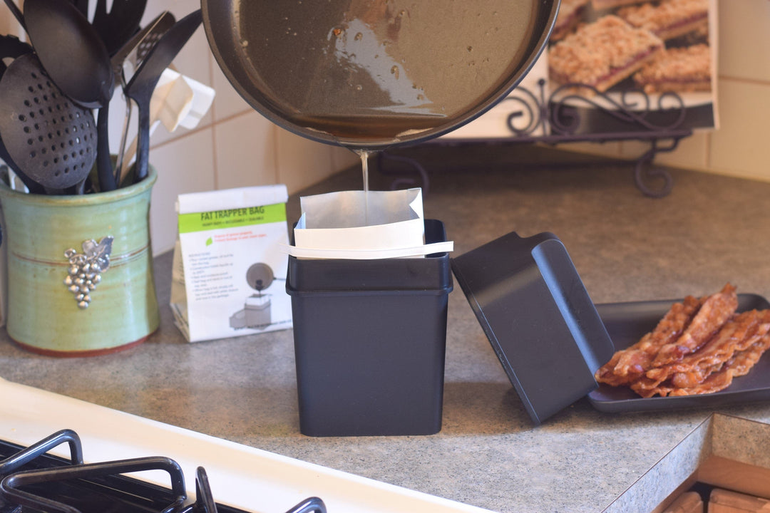 Warm grease being poured from a skillet into a Fat Trapper disposal bag beside a kitchen stove instead of down the sink drain