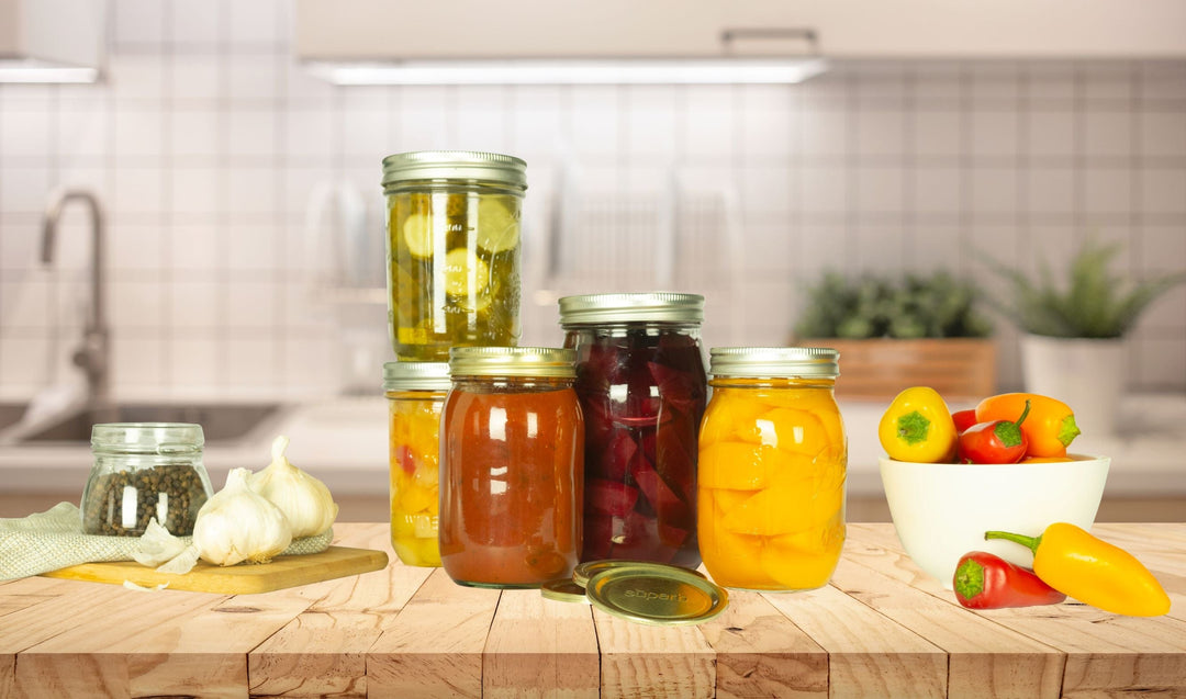 Wide mouth mason jars of peach halves, beets and whole peppers on a kitchen counter, showing the straight-sided profile